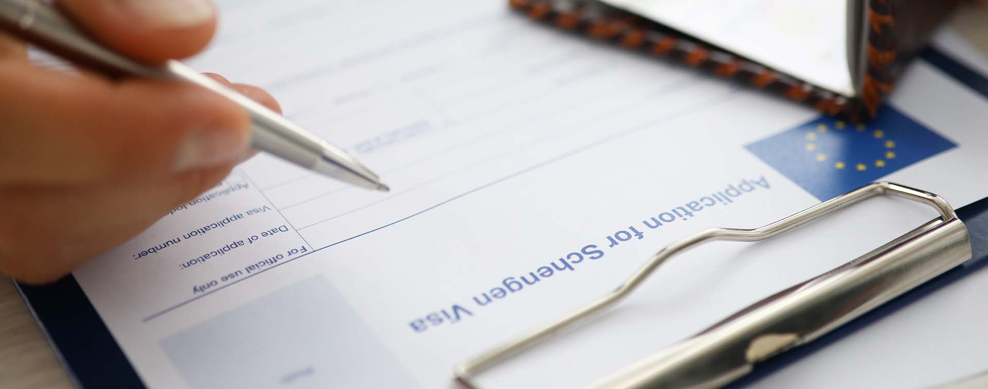 Male hand holding silver pen with passport filling in a form