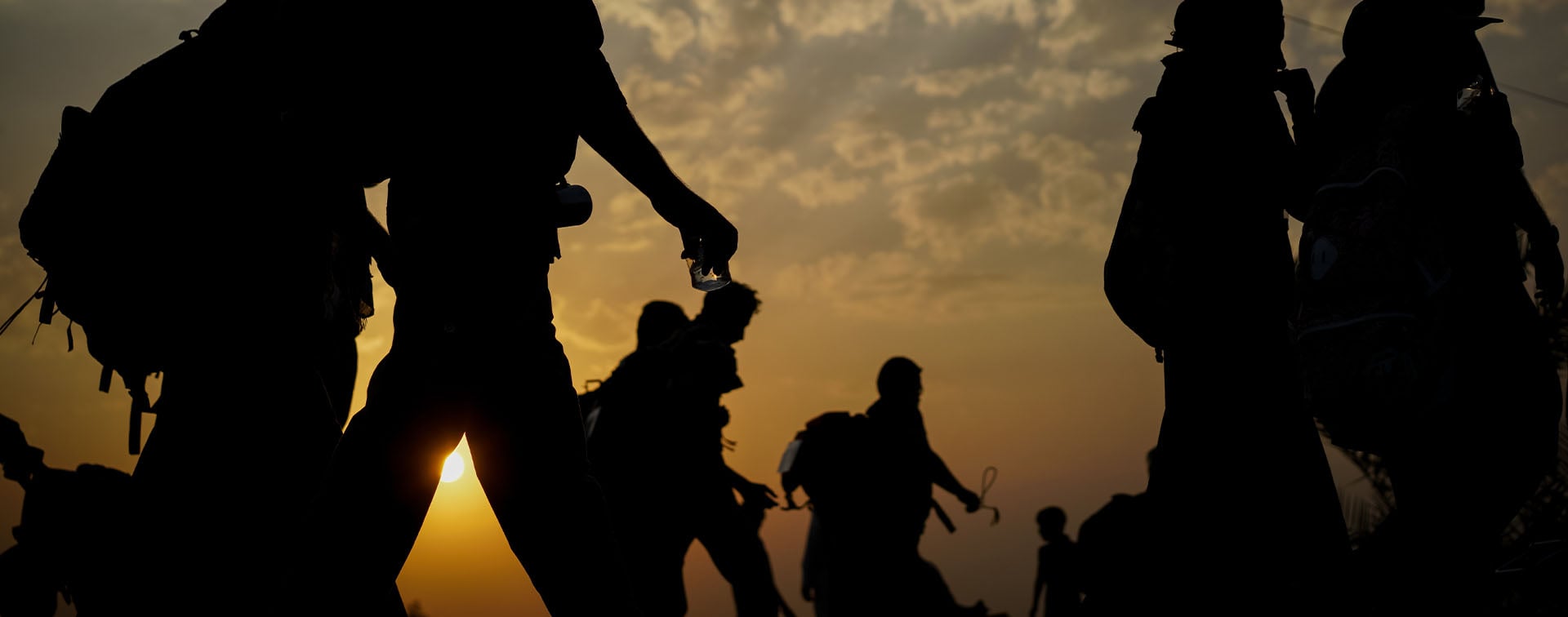 Group of immigrants carrying backpacks and walking at sunset