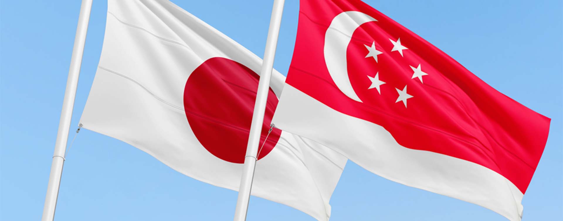 Singaporean and Japanese flags flying over a clear blue sky