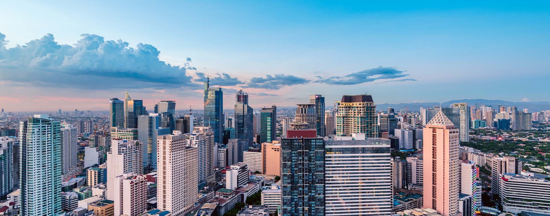 Manila’s skyline filled with tall buildings, cast in pink light by sunset, with clouds in the background
