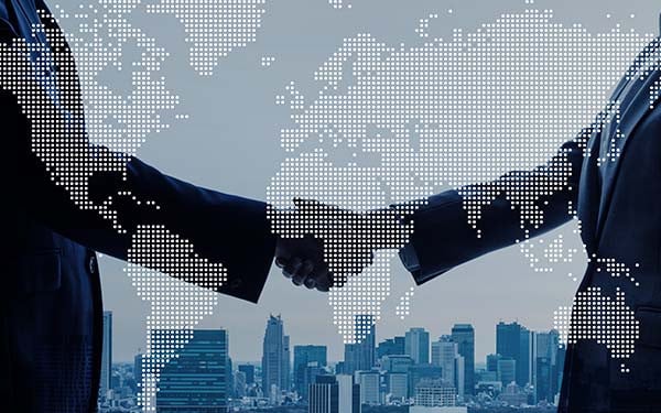 Businesspeople shaking hands with world map superimposed and cityscape in the background