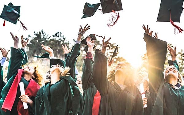 Large group of happy college students celebrating their graduation day outdoors while throwing their caps up in the air