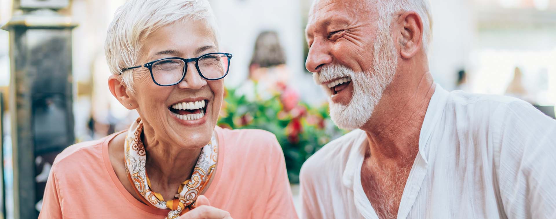 An attractive affluent senior couple laughing while sitting outside at a restaurant