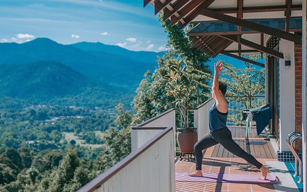 A woman practising yoga on a balcony overlooking a valley and mountains
